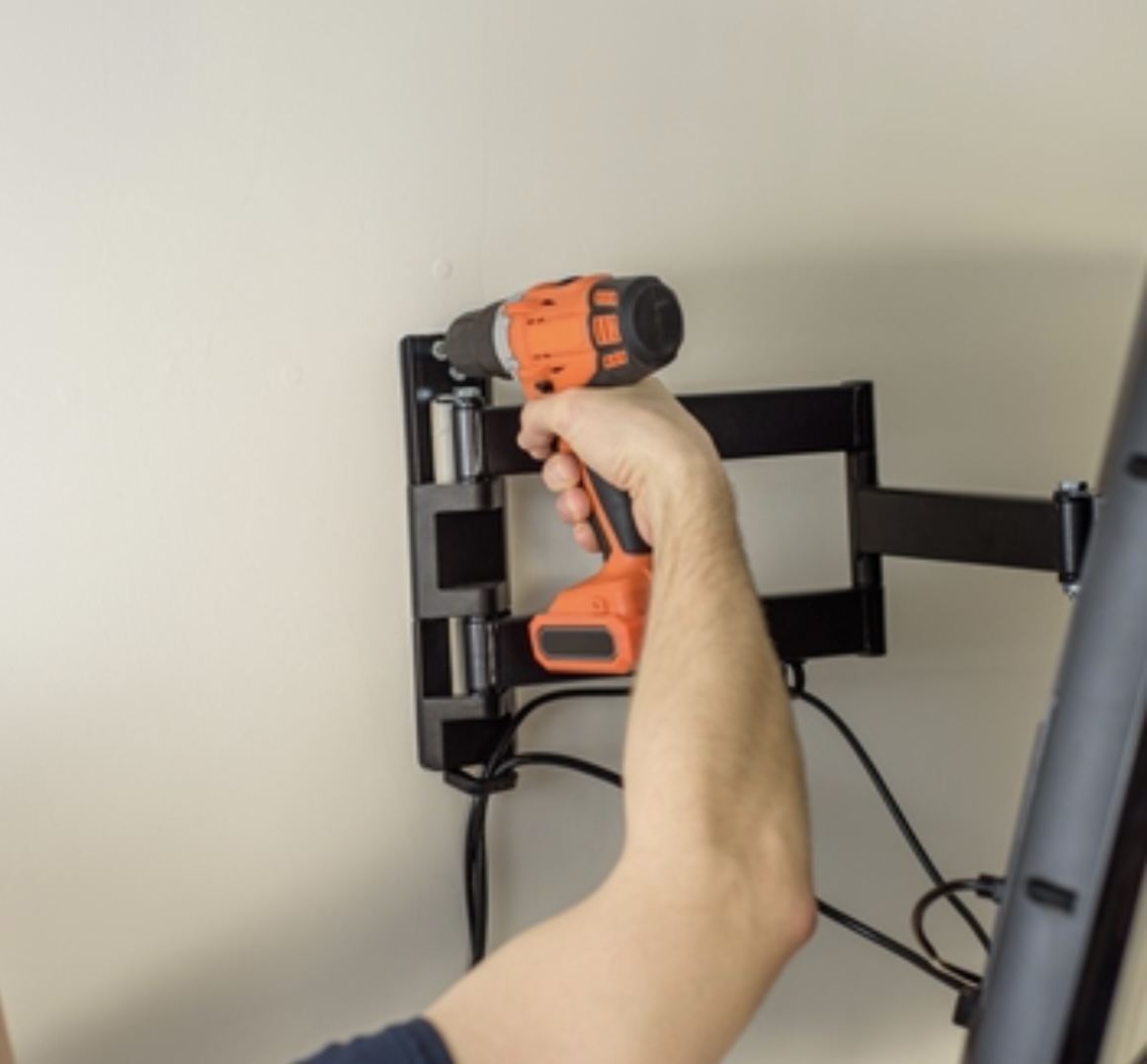 Technician using a drill to secure a swivel TV wall mount bracket onto drywall